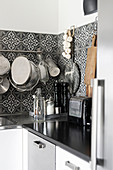 Kitchen utensils hung from rod on ornate, black-and-white, tiled splashback