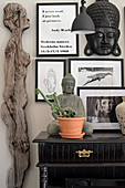 Weibliche Figur aus Holz neben Konsolentisch mit Buddhafigur und schwarz gerahmten Fotos und Botschaft an der Wand