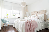 Double bed with button-tufted headboard in bedroom in white and pastel shades