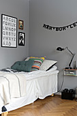 Buchstabengirlande über dem Bett mit Volant vor grauer Wand