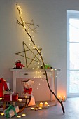 Stimmungsvolle Weihnachtsdekoration: LED-Lichterkaskade am Ast, Sterne aus Weidenästen, Teelichter, Kerzen und Weihnachtsgeschenke