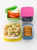 A packed lunch with chicken, vegetables, blueberries and crackers