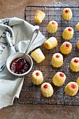 Mini jam sandwich cakes on a cooling rack with a bowl of jam