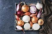 Variety of whole and sliced red, white, yellow and shallot onions on wooden square tray