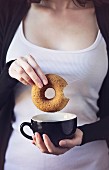 Breakfast time: woman holding in her hands a donut and a cup of coffee