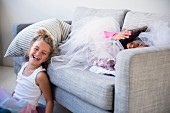 Zwei Mädchen in Tüllröcken spielen und lachen auf einem Sofa