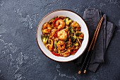 Udon stir-fry noodles with shrimp in bowl and chopsticks on dark stone background copy space