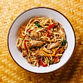 Udon stir-fry noodles with chicken meat and sesame in bowl on bamboo tray background close-up