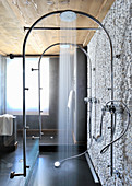 Rainfall showers fitted on arched pipes next to stone wall clad in white pebbles
