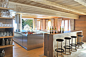 Barstools at counter in front of open-plan stainless-steel kitchen