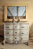 Chest of drawers with handles made from branches below mirror on wooden wall