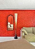 Designer-Stehlampe und Sofa vor rot gestrichener Ziegelwand mit Spiegel