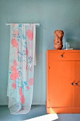 Delicate floral fabric hanging next to orange cabinet