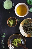 A cup of matcha latte, a cup of green tea, matcha powder in a small bowl and green tea on a dark background