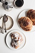 Two butter croissants, one almond croissant, one black coffee, a small plate with spoons and a butter knife arranged on a white tabletop