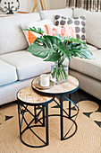 Two-part side table with lantern and philodendron leaves in front of upholstered furniture