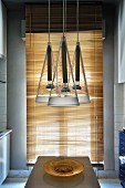 Glass lampshades above dining table in front of lowered louvre blinds