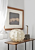 Framed picture above lampshade and sculpture on vintage table