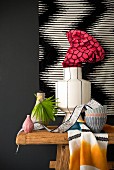Stillleben mit Vasen und Schüsseln auf Holztisch vor schwarz-weisser Wanddekoration