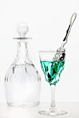 Absinth mit Absinthlöffel im Kristallglas vor Kristallkaraffe mit Wasser