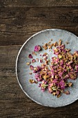 Dried edible pink rose petals on a grey plate on a wooden surface