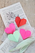 Origami-Herzen und Federn auf Buchseiten und Seidenpapier