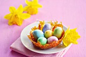 A caramel nest with colourful sugar eggs on a plate, and daffodils in the background