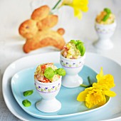 Potato salad with carrot, apple, peas and mayonnaise served in egg cups, with a yeast bread Easter bunny and daffodils in the background