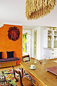 Wooden table and chairs on colourful rug and purple bench against orange wall