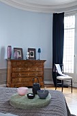 Teapot on round raffia cushion in front of antique chest of drawers