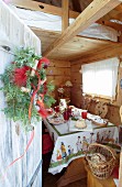 View of set table in wooden cabin seen through open wooden door with wreath