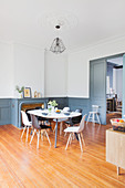 Dining table and chairs in front of fireplace in interior with white walls and dove grey wainscoting