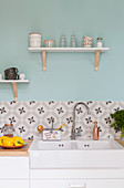 Peppers and jars on wooden worksurface with cement-tiled splashback below cups on bracket shelves on pale blue wall