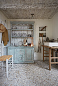 Rustic wooden table with countertop sink and dresser in small room with pebble-cobbled floor