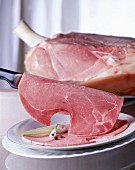 A piece of ham with a knife and sliced ham on a plate