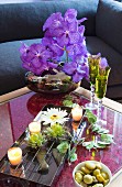 Arrangement of artificial flowers, bowl of water and tealights on coffee table