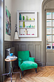 Emerald velvet armchair against grey wainscoting and below wall-mounted display case