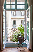 Watering can on stool in front of open balcony doors with view of house opposite