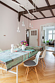 Colourful tablecloth on long table, classic chairs and pendant lamps with light bulbs in dining room