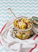 Spaghetti with brussels sprouts and bacon in a glass jar with a fork