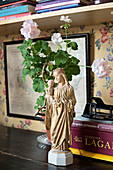 Heiligenfigur vor einer Geranie und Büchern auf dem Schreibtisch