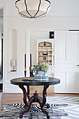 Round wooden table on zebra-skin rug in front of open panelled door