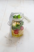 A pasta salad with cocktail tomatoes, rocket and mountain cheese in a glass jar with a fork
