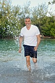 A man with grey hair wearing a white T-shirt and dark blue shorts running through water