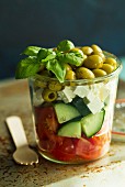 A salad of tomatoes, cucumbers, feta, green olives and basil in a glass