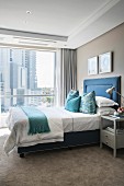 Bed with upholstered blue frame and beige carpet in elegant bedroom