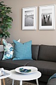 Grey sofa with turquoise scatter cushions below framed photos on beige wall