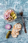 A sausage, red onion and gherkin salad in a glass, with baguette slices