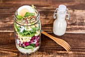 Orzo pasta with lambs lettuce, radicchio, endive, croutons, cheese, walnuts and eggs in a glass jar with dressing and a wooden fork