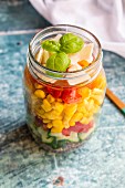 A colourful salad in a glass jar with red quinoa, cucumber, peppers, corn, tomatoes, pecorino and basil